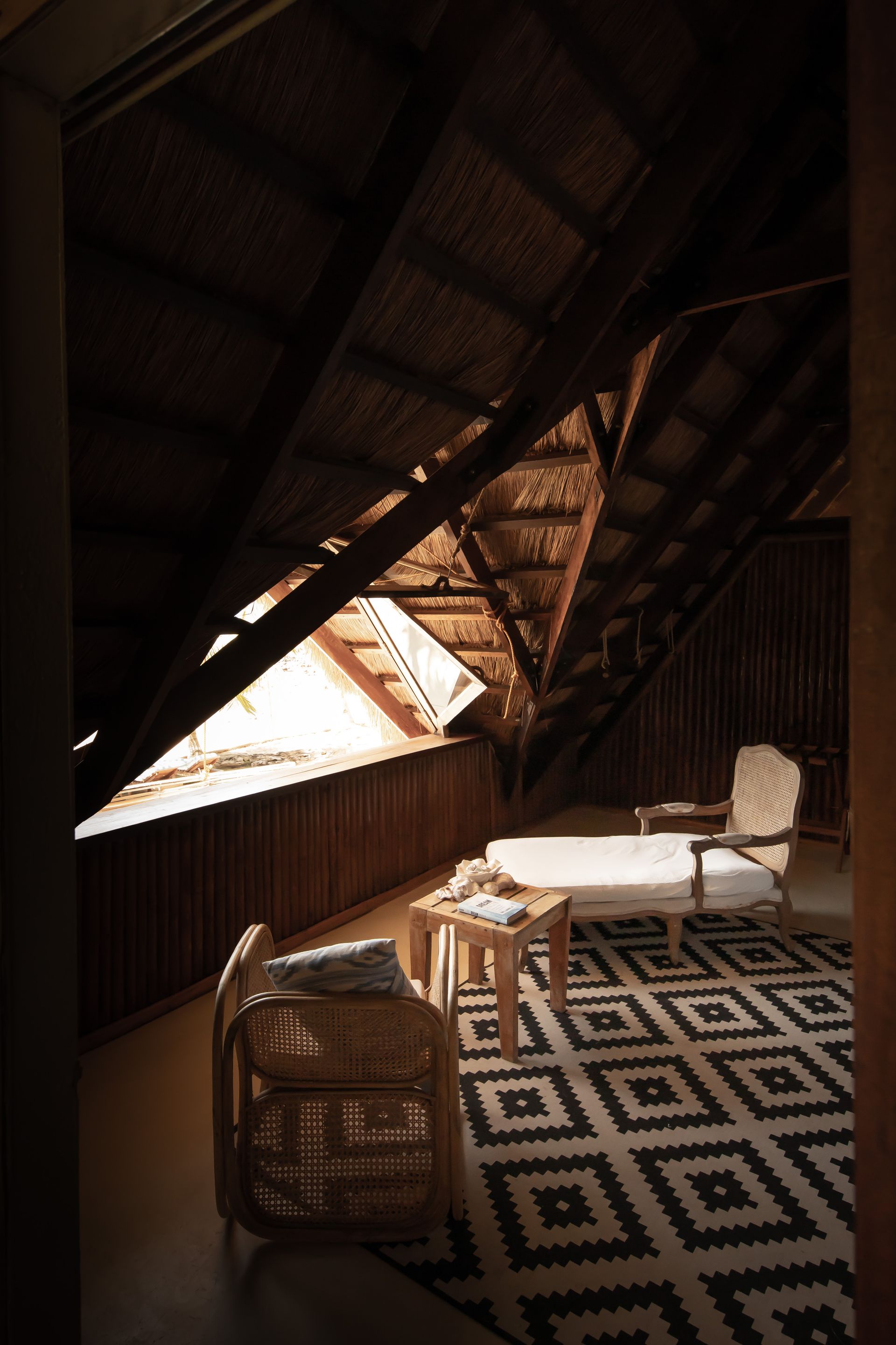 An attic with a rug , chair , table and stairs.