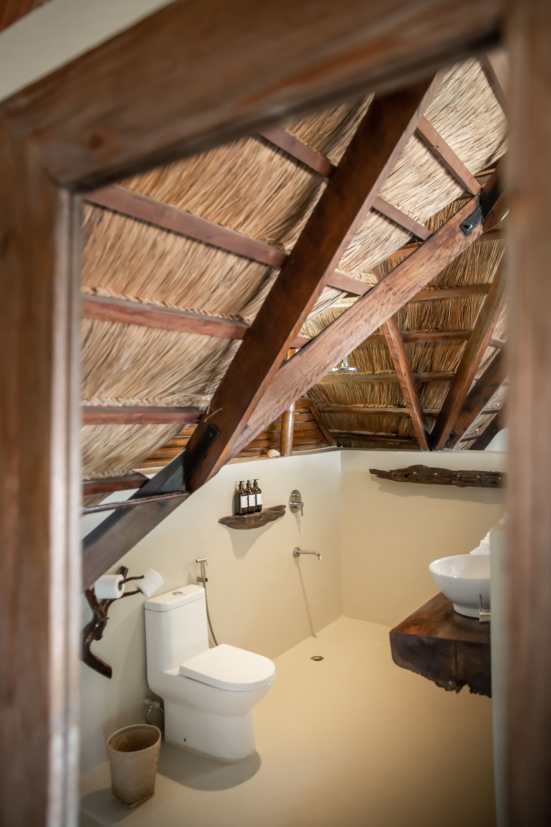 A bathroom with a toilet , sink and thatched roof.