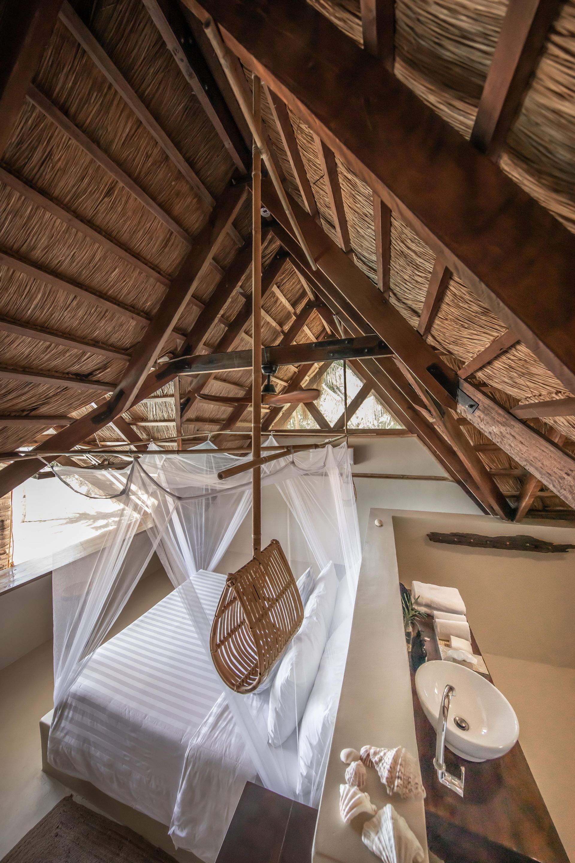 A bedroom with a thatched roof , a bed and a sink.