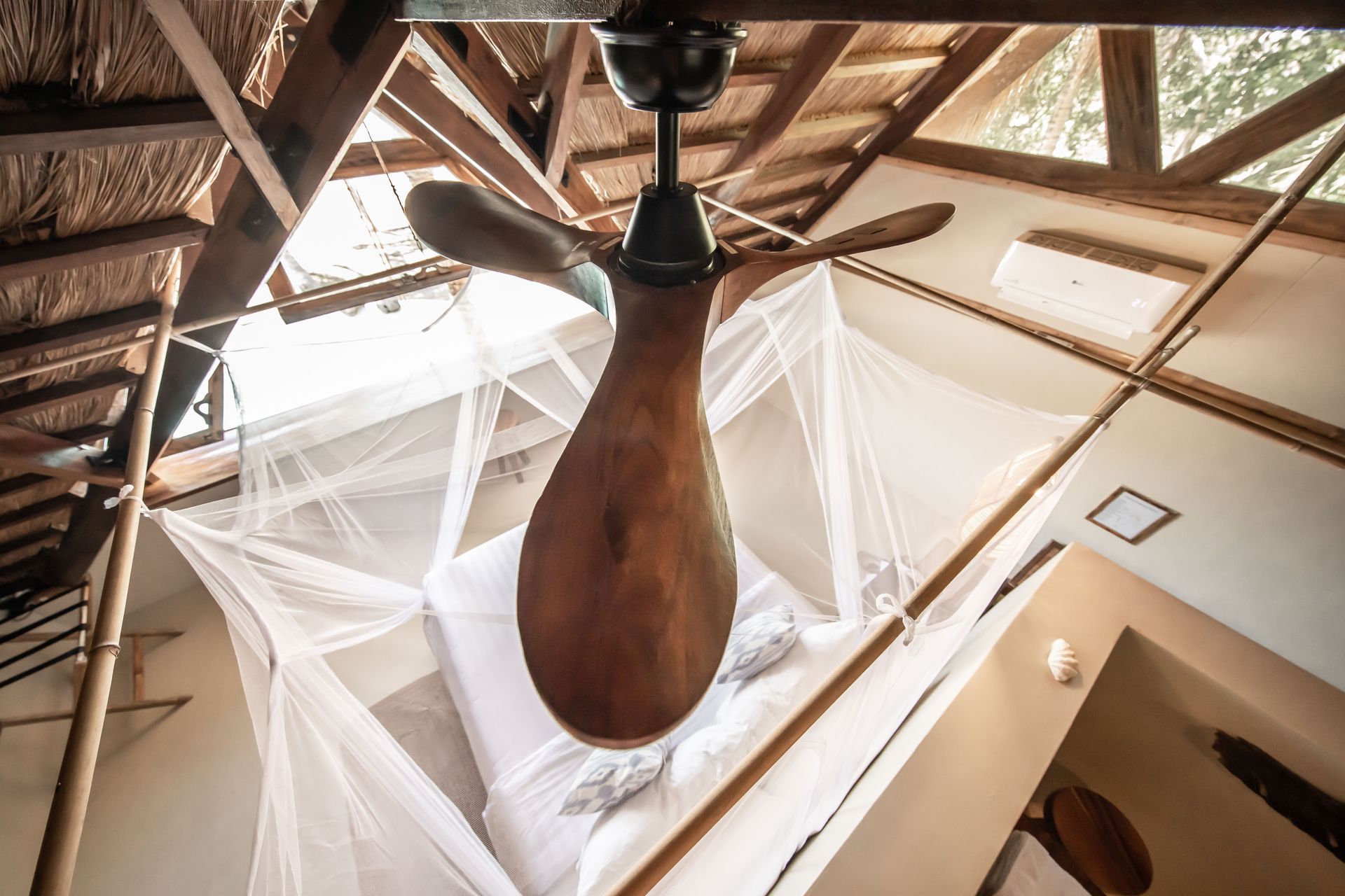 A wooden ceiling fan is hanging from the ceiling above a bed.