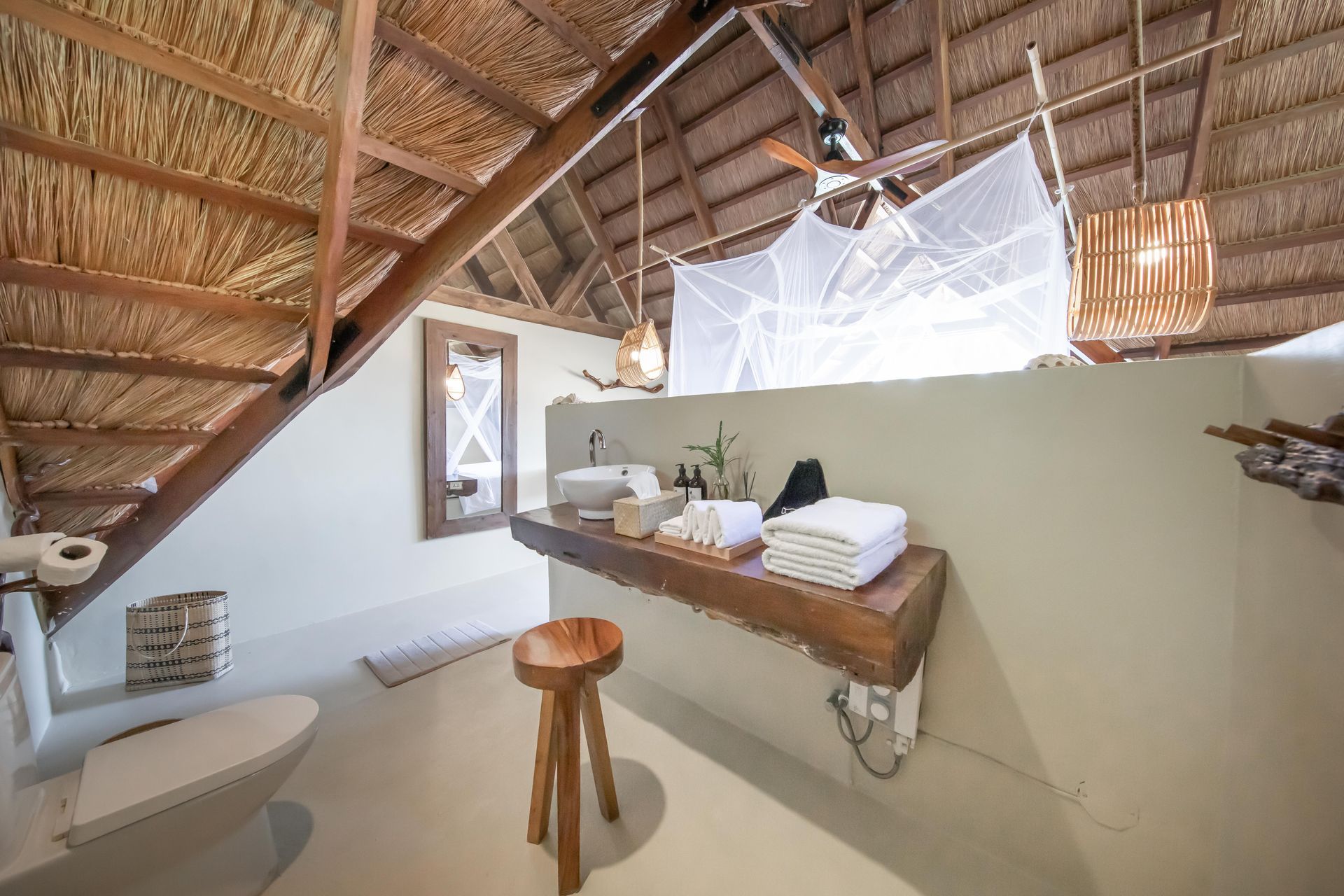 A bathroom with a toilet , sink , mirror and stools.