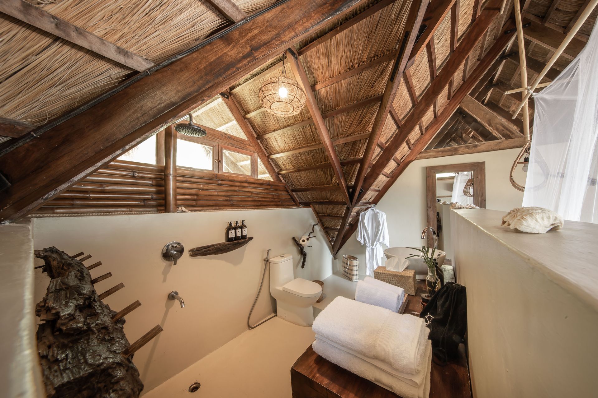 A bathroom with a toilet , sink , and thatched roof.