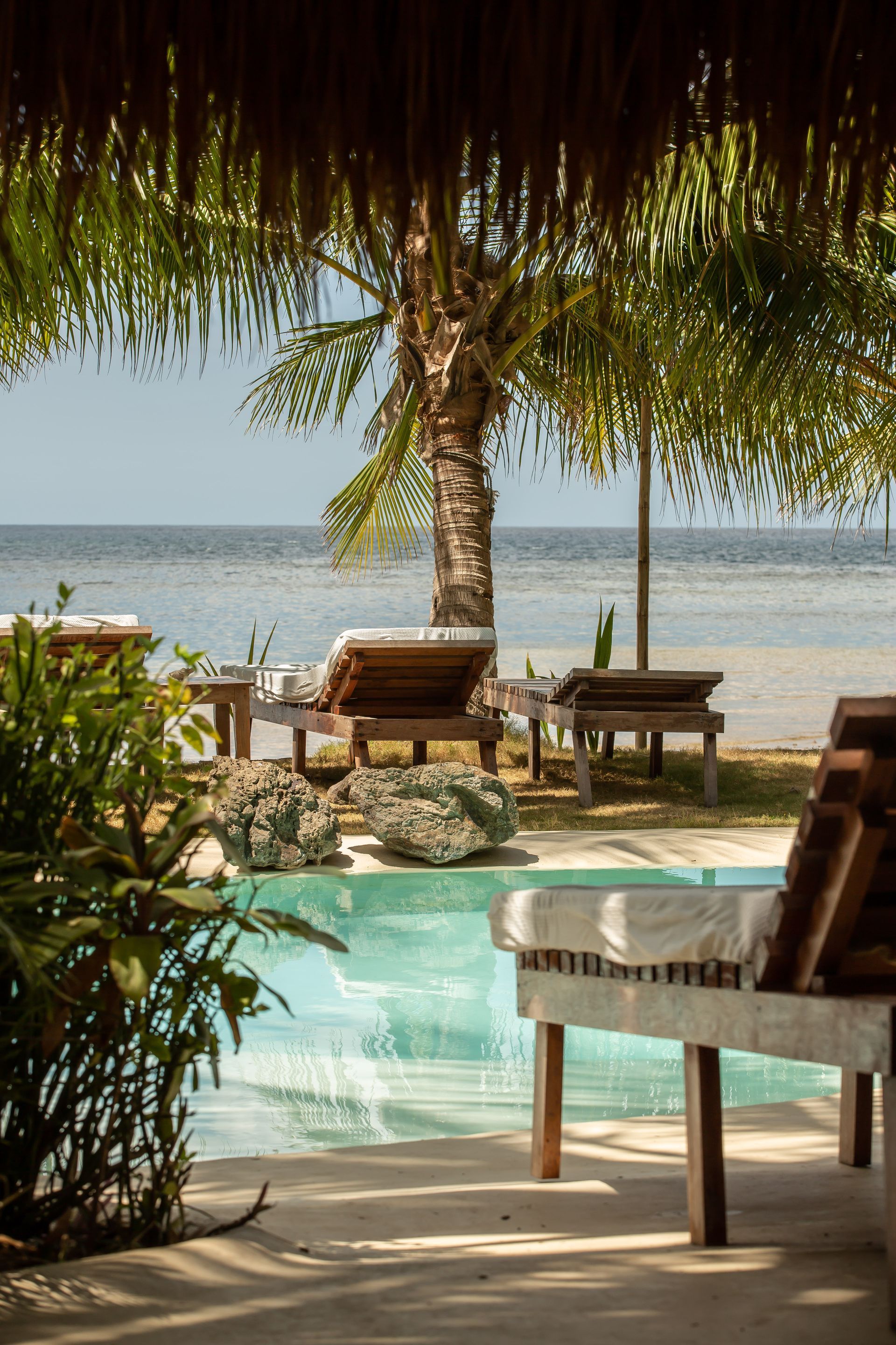 A swimming pool surrounded by chairs and umbrellas with a view of the ocean.