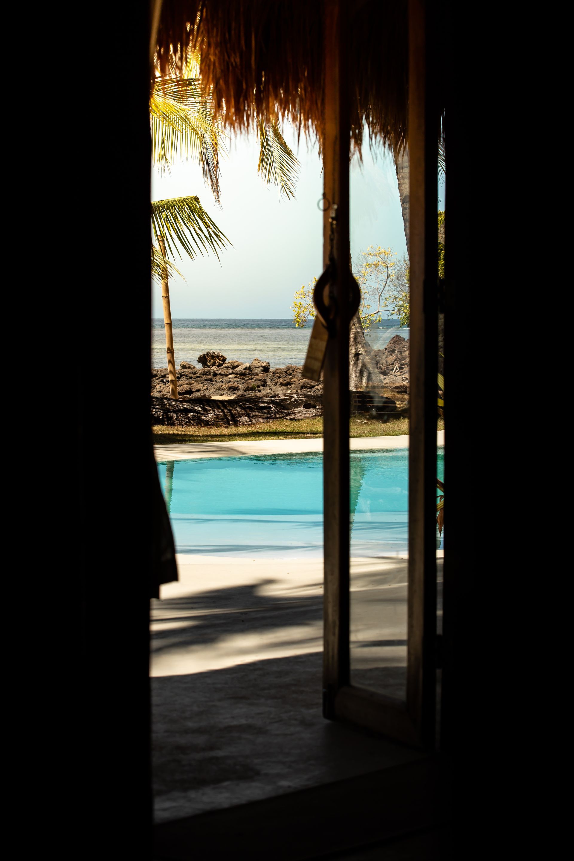 A doorway leading to a swimming pool with a thatched roof.