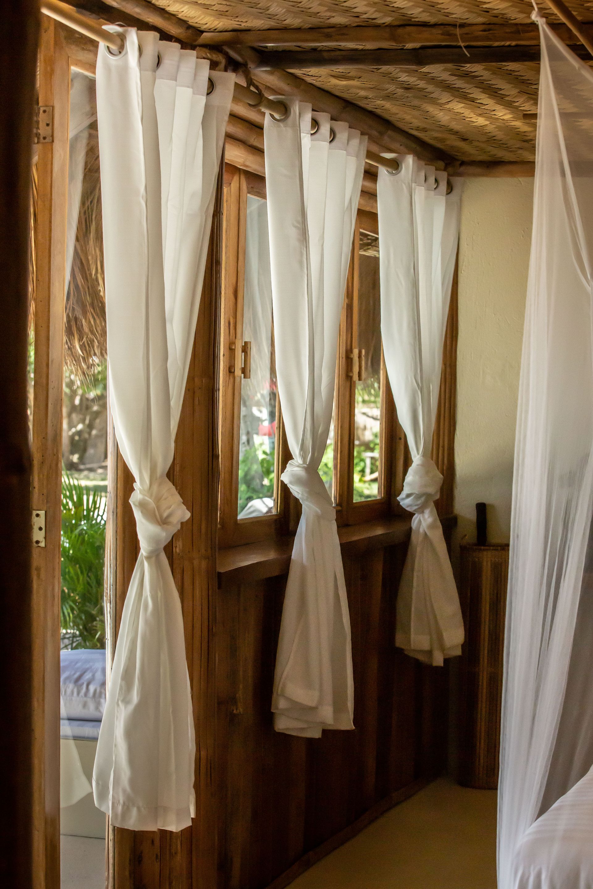 A bedroom with a canopy bed and white curtains on the windows.