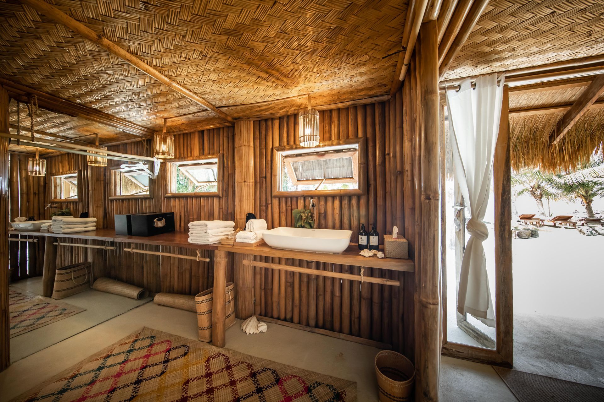 A bathroom in a thatched hut with a sink and mirrors.