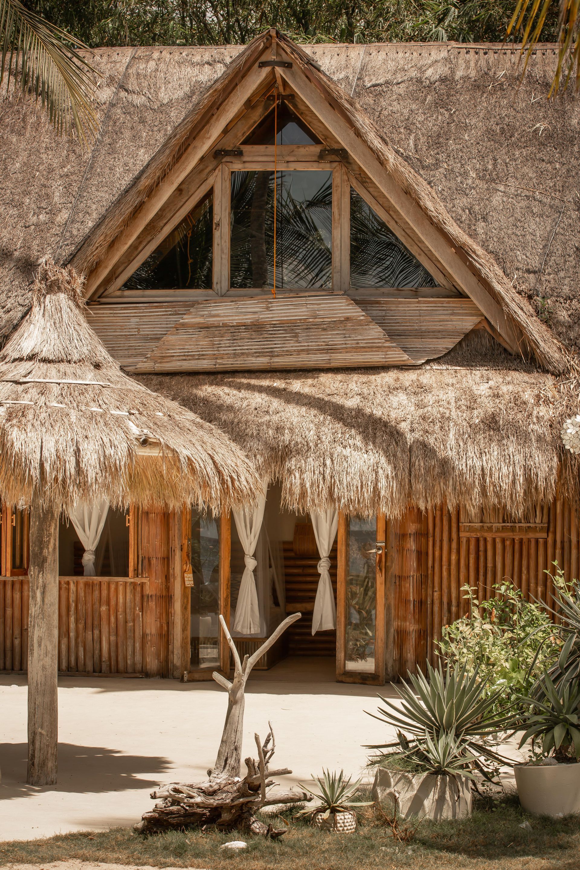 A wooden house with a thatched roof and a large window.