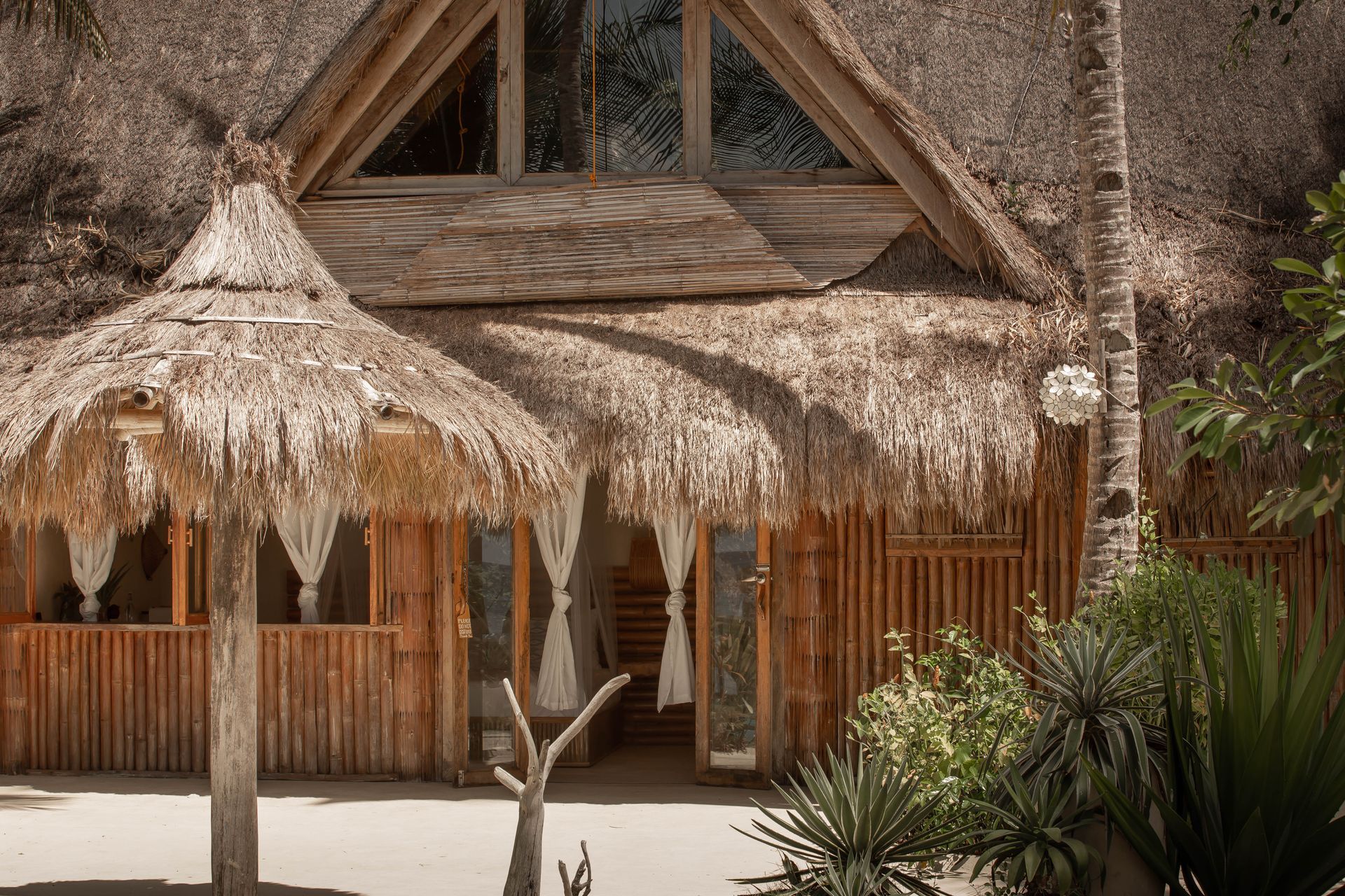 A wooden house with a thatched roof and umbrellas in front of it.