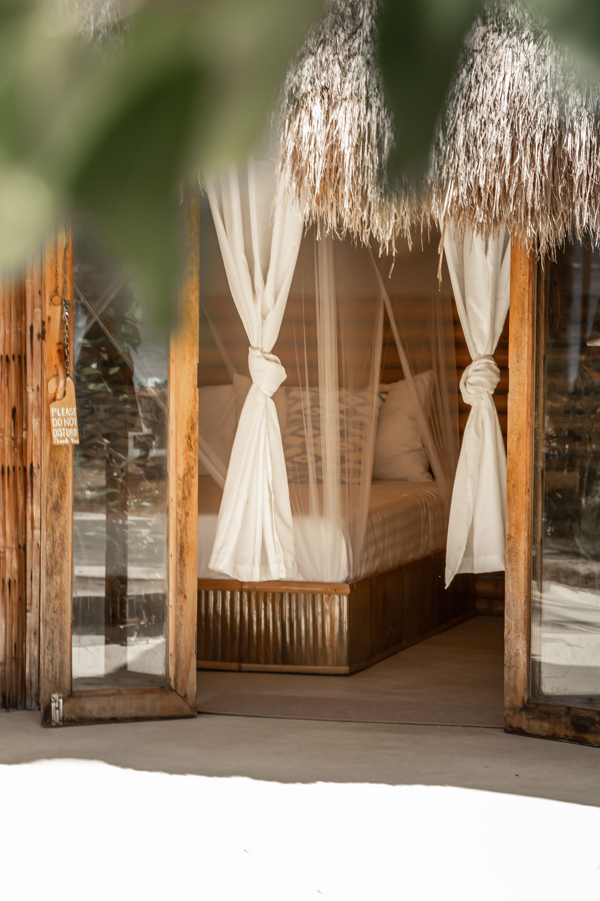 A bed with a canopy and white curtains is sitting in front of a wooden building.