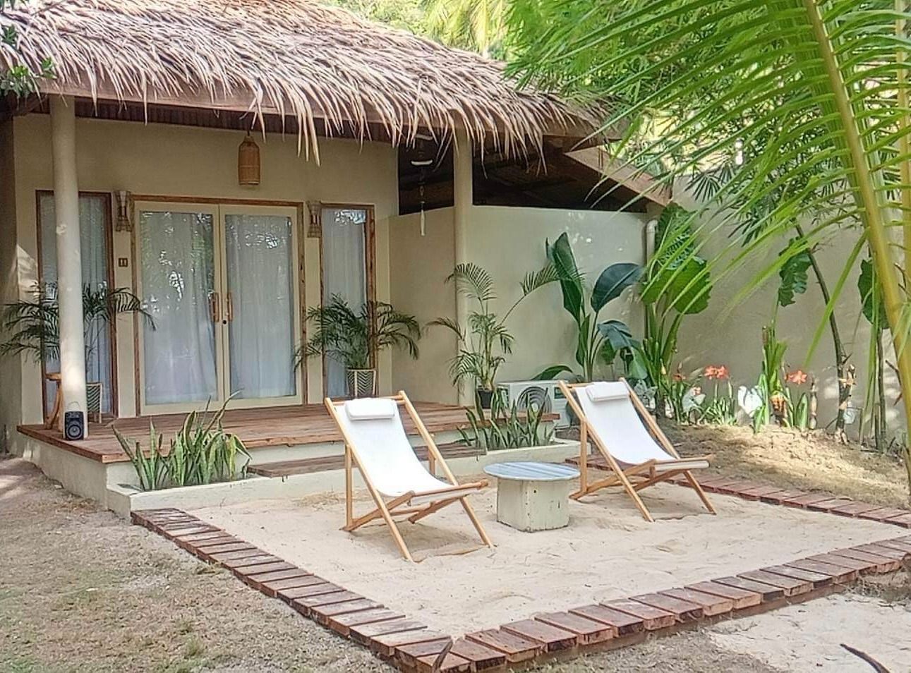 Two chairs are sitting in front of a house with a thatched roof.