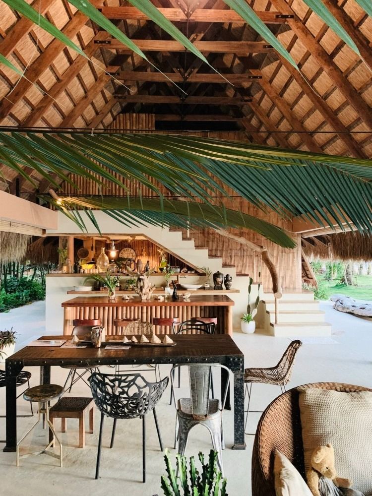A dining room with a table and chairs under a thatched roof.
