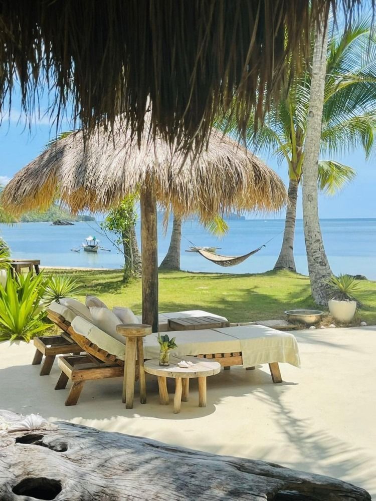 A thatched umbrella is sitting on a beach next to a hammock.
