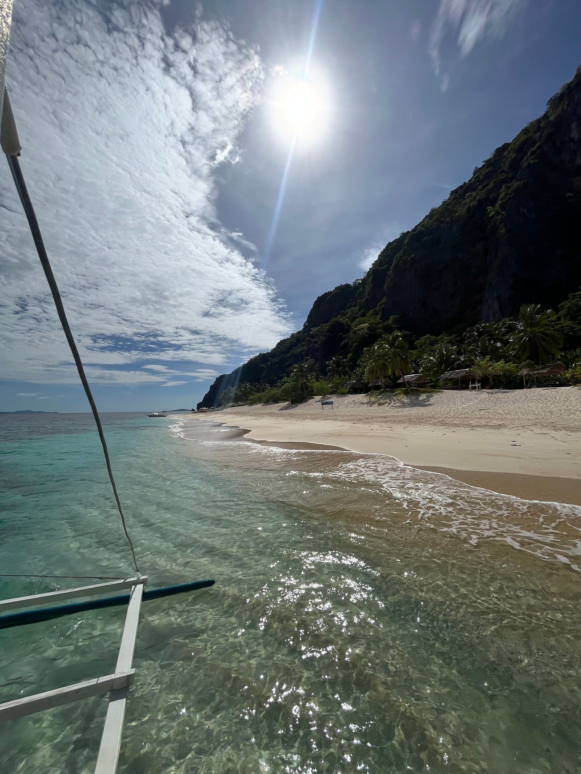A view of a beach from a boat with the sun shining through the clouds