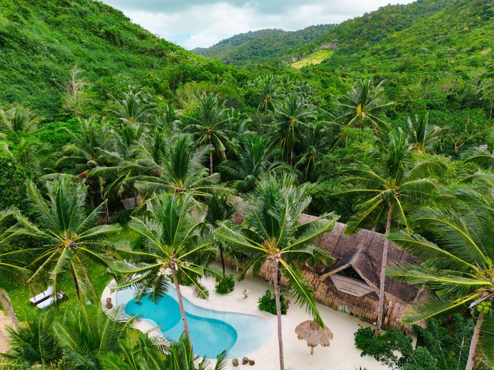 An aerial view of a tropical resort with a swimming pool surrounded by palm trees.