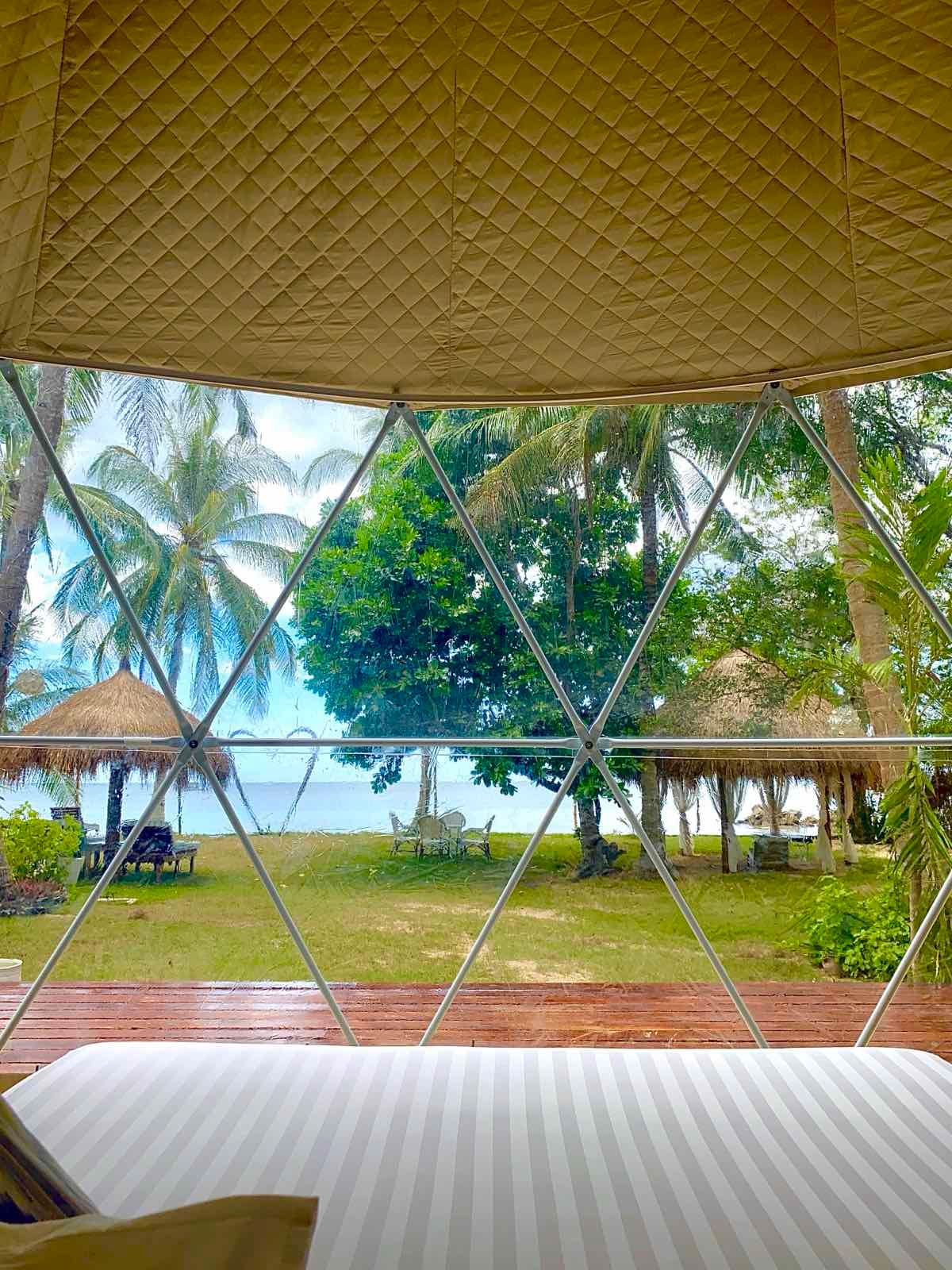 A bed in a dome with a view of the ocean and palm trees.
