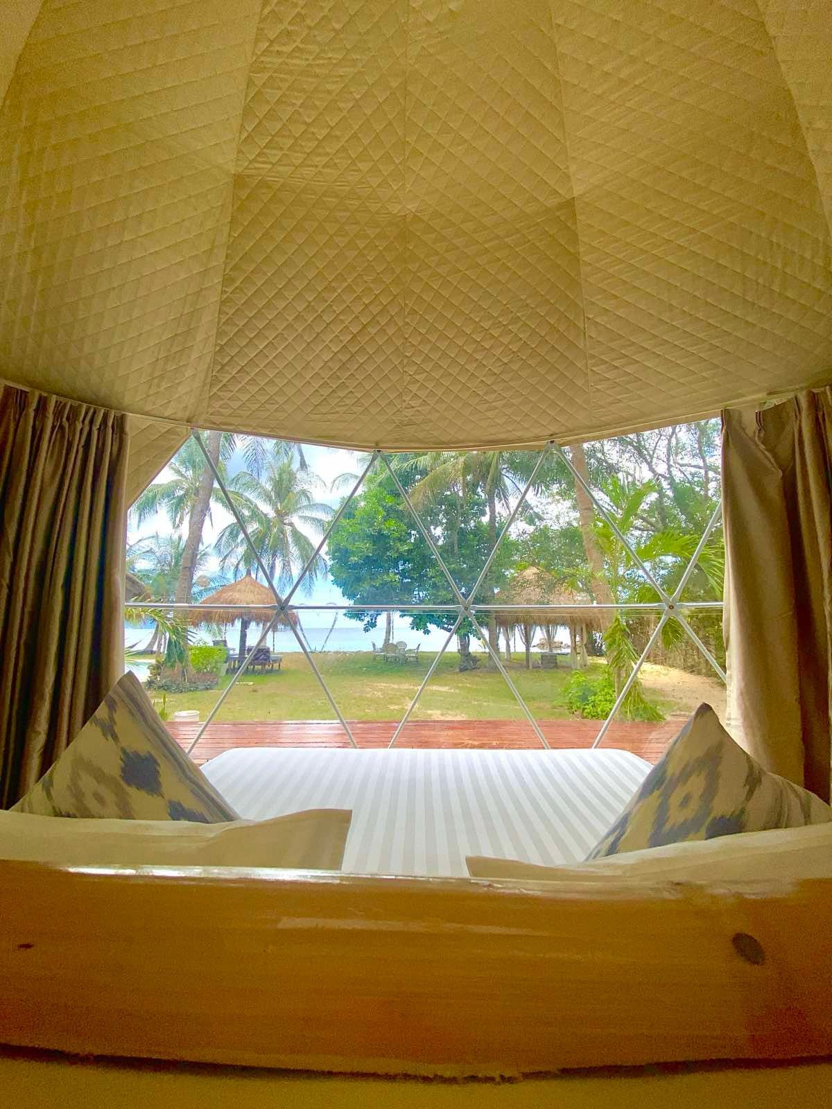 A bed in a tent with a view of the ocean.