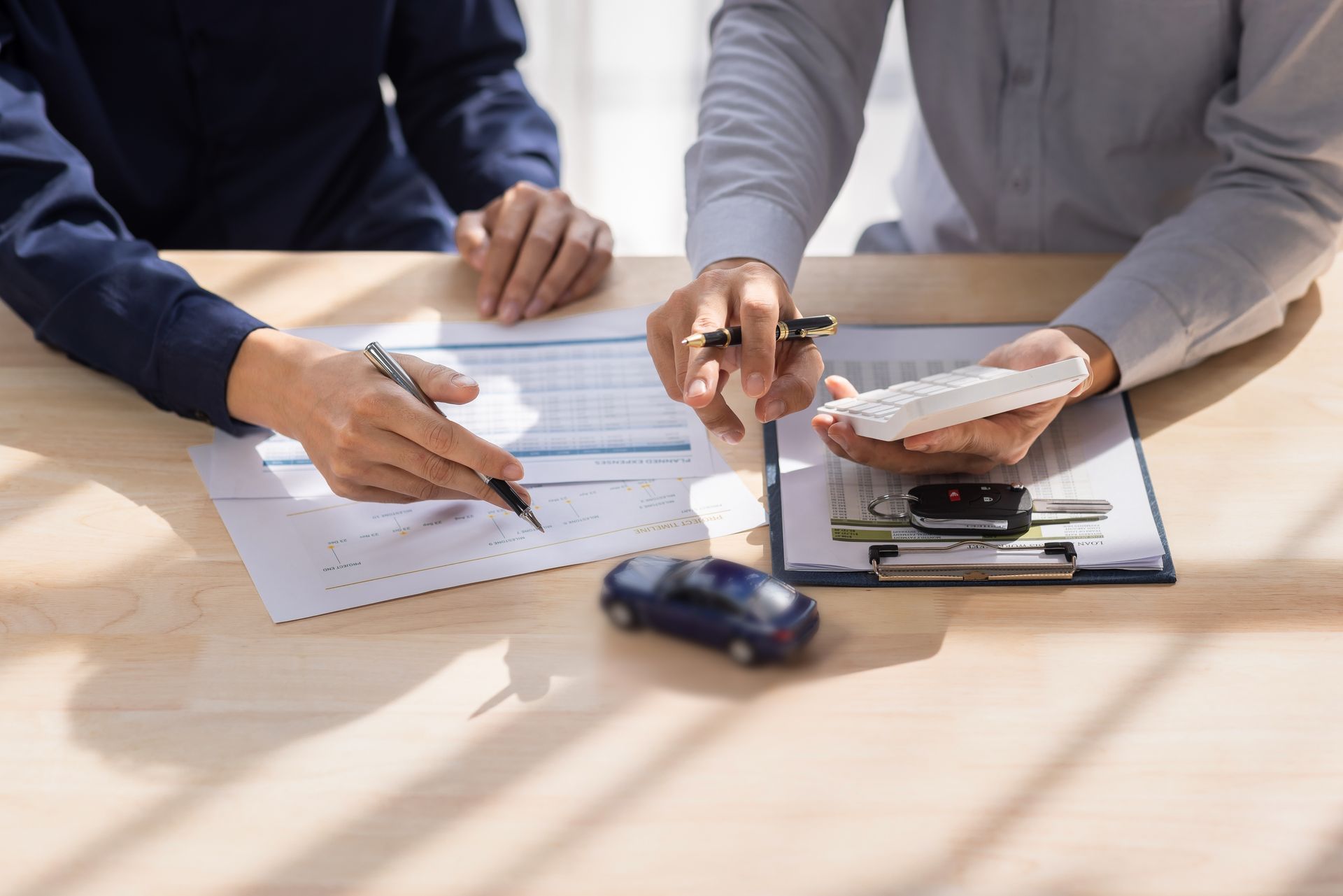 Clients reviewing car insurance forms with a calculator and model car. Clients reviewing car insurance forms with a calculator and model car.