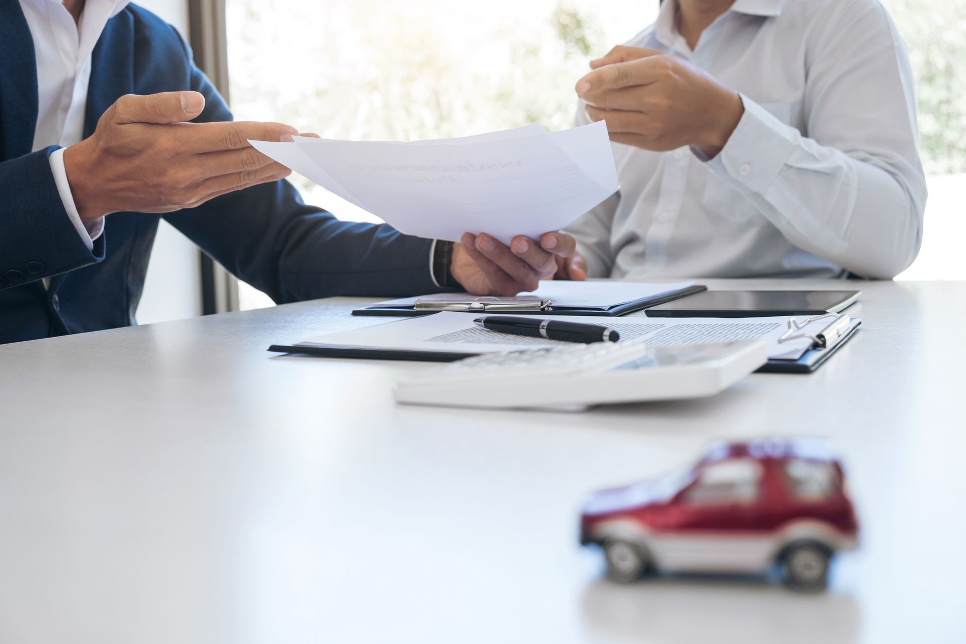 Business meeting with documents and toy car on table, close-up of hands and office supplies.