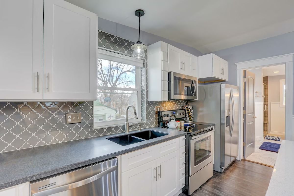 Bright kitchen with white cabinets, gray countertops, stainless appliances, and a patterned tile backsplash