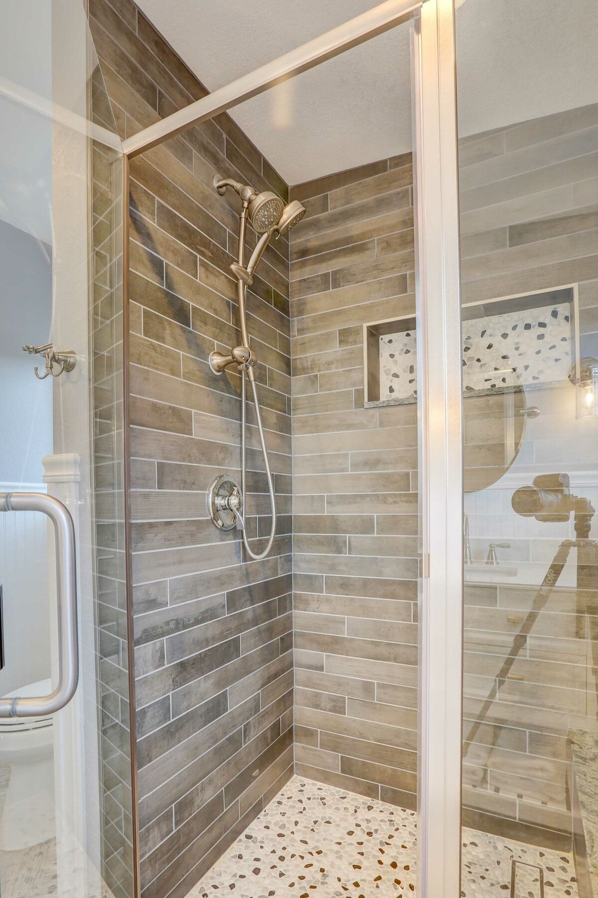 Modern tiled walk-in shower with glass door, rain showerhead, and pebble floor tiles.