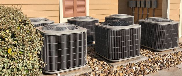 A row of air conditioners are sitting in front of a house.