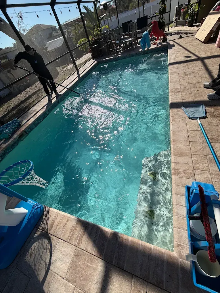Backyard swimming pool with blue water, lounge chairs, and people standing near the far end
