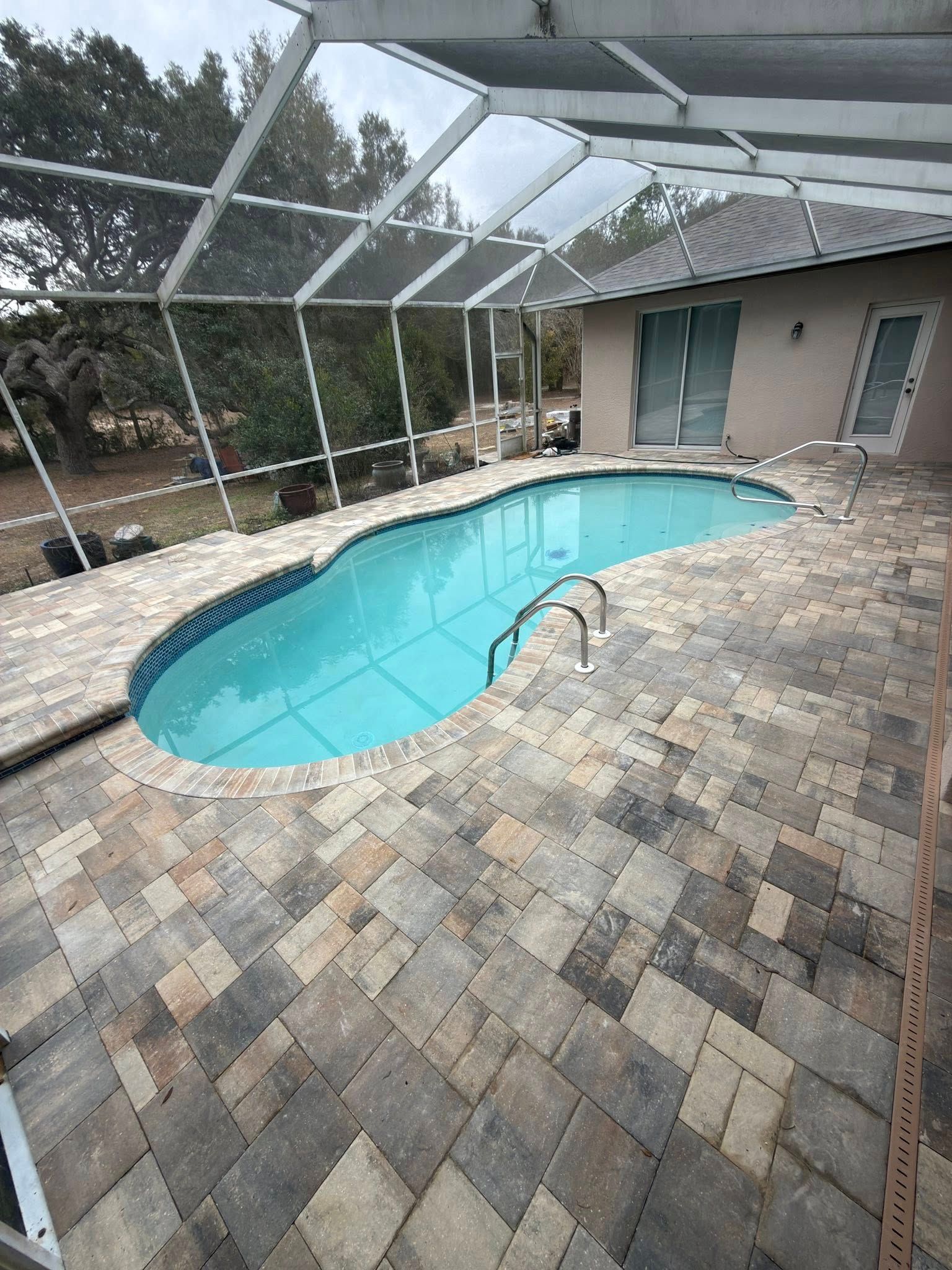 Screened backyard patio with a small turquoise pool and stone pavers beside a house
