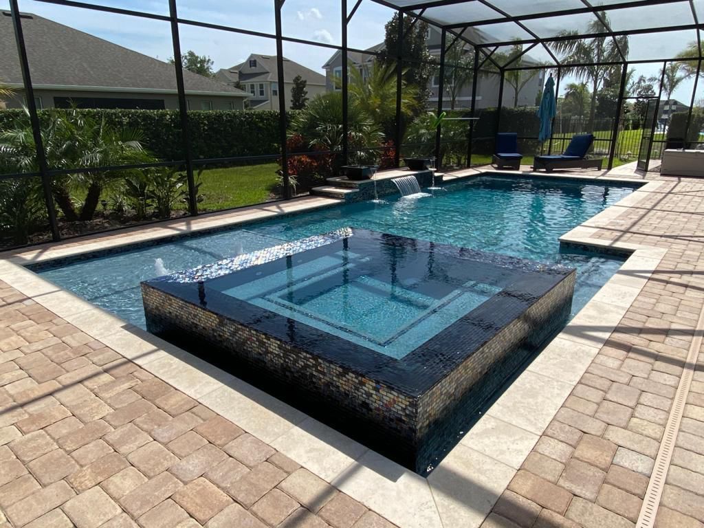 Backyard pool with raised spa, blue water, and stone deck in bright sunlight