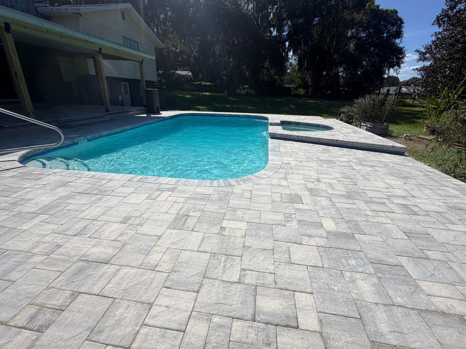 Sunlit backyard pool with turquoise water and a light gray stone patio