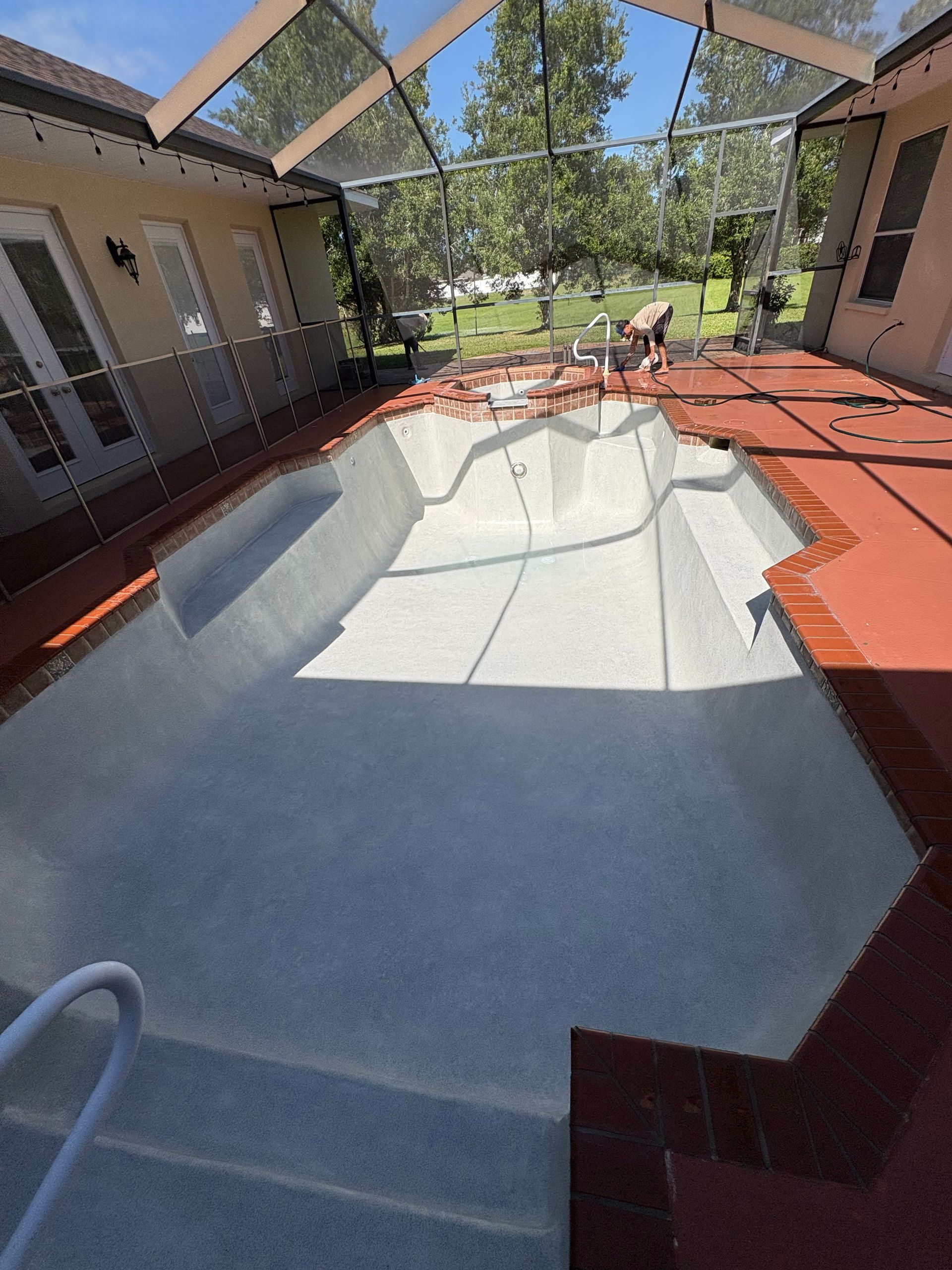 Empty backyard pool with white liner, red deck, and patio furniture under a screened enclosure