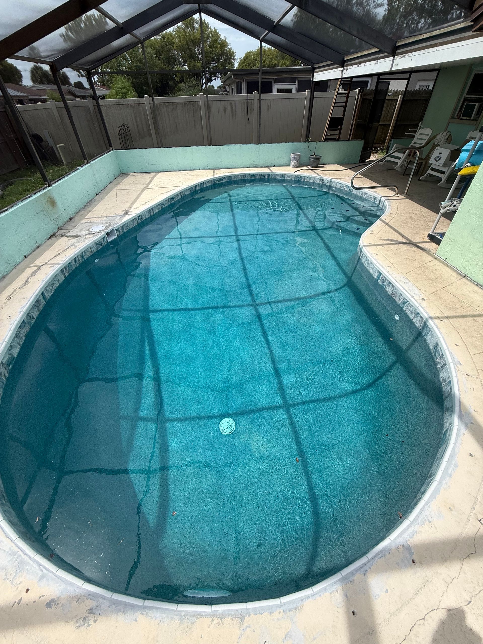 Small backyard swimming pool with clear blue water under a screened patio canopy.