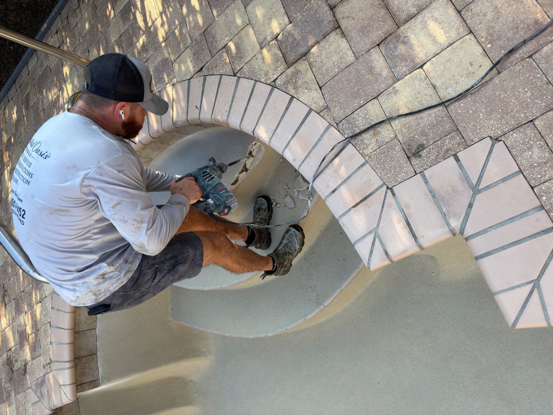 Worker power-washing a tiled pool basin with a pressure washer.