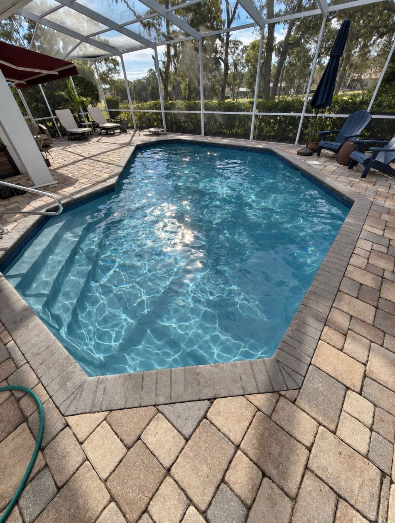 Screened backyard pool with blue water, brick pavers, and lounge chairs under a covered patio.