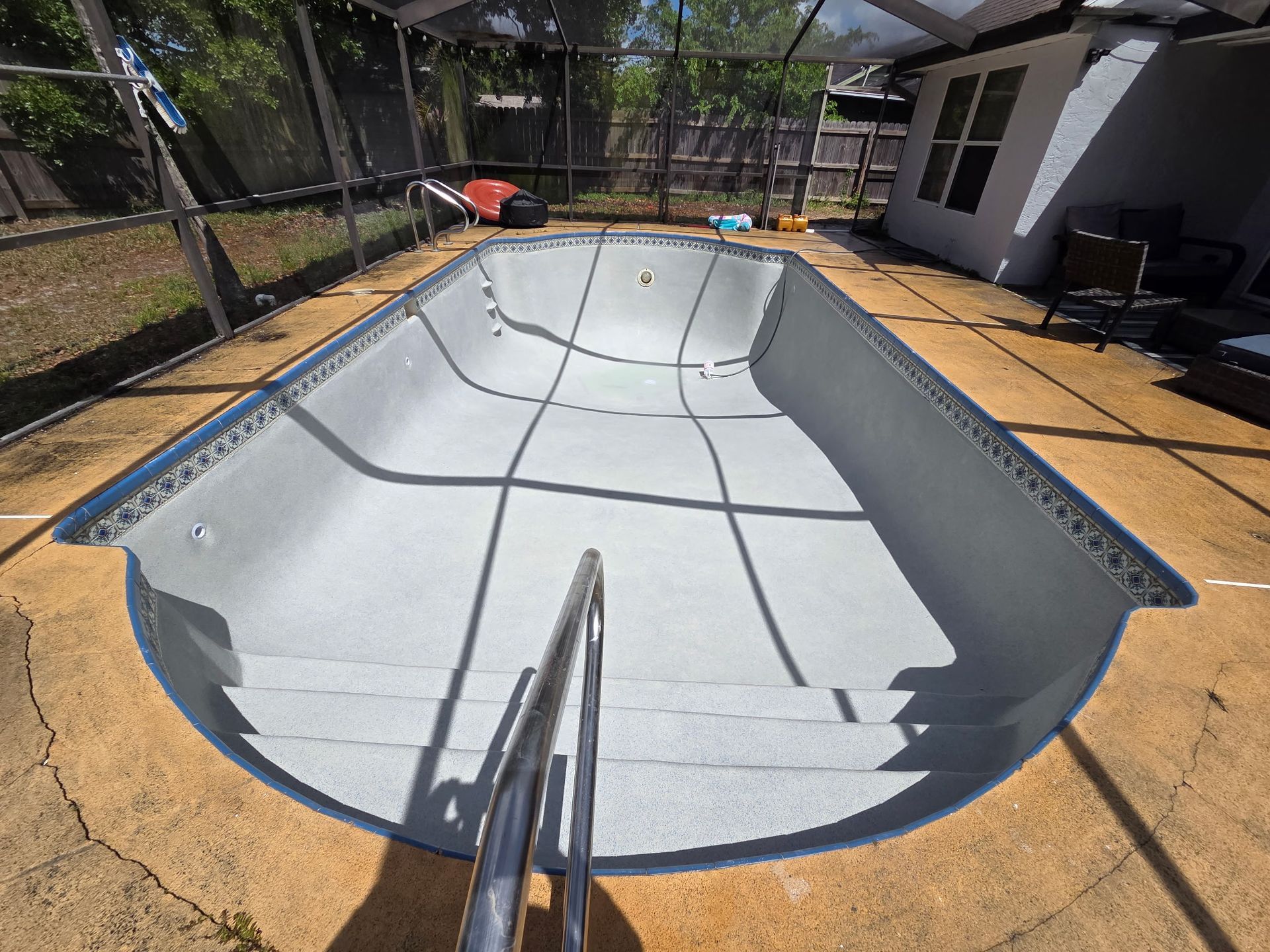 Empty backyard swimming pool under construction, with gray resurfaced interior and surrounding patio.