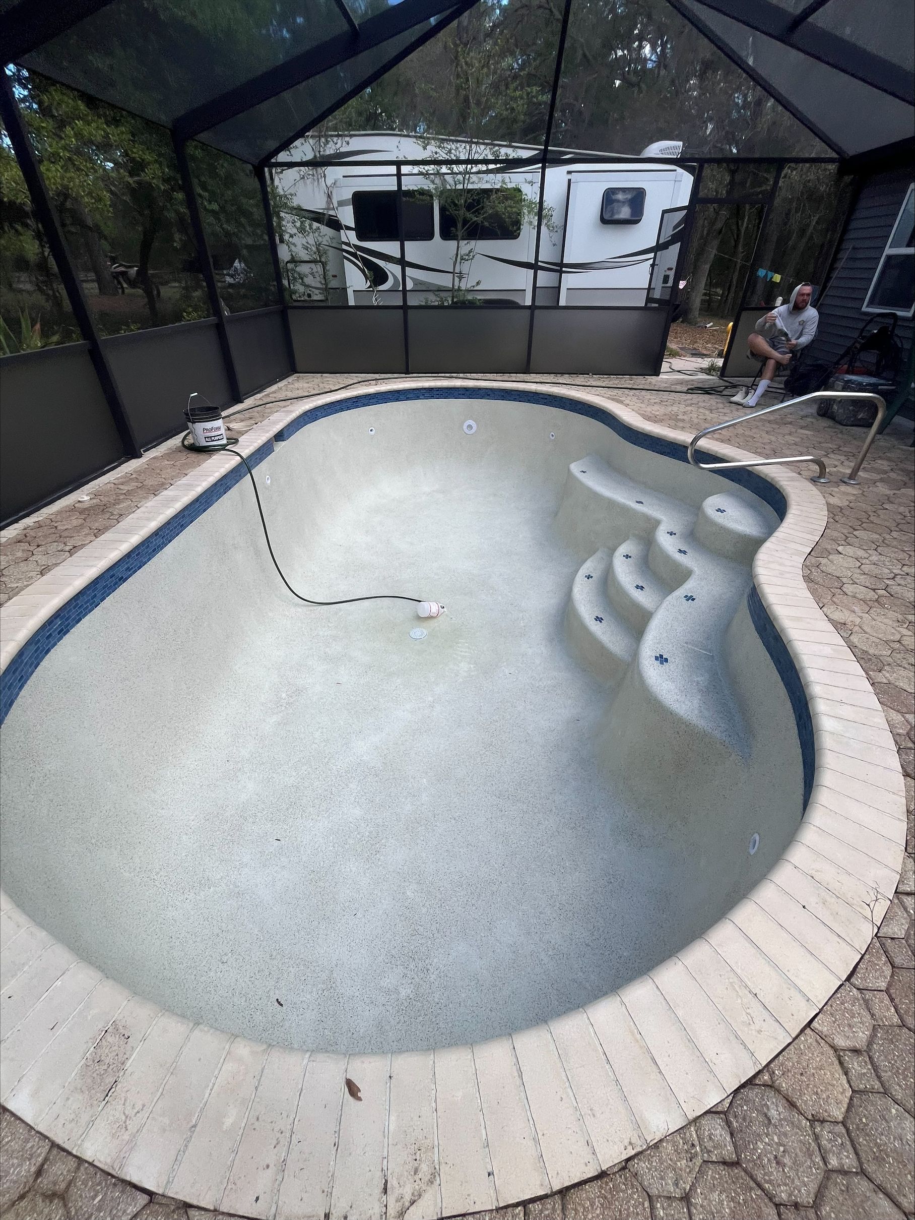 Empty backyard swimming pool with a blue hose inside, surrounded by a screened enclosure.