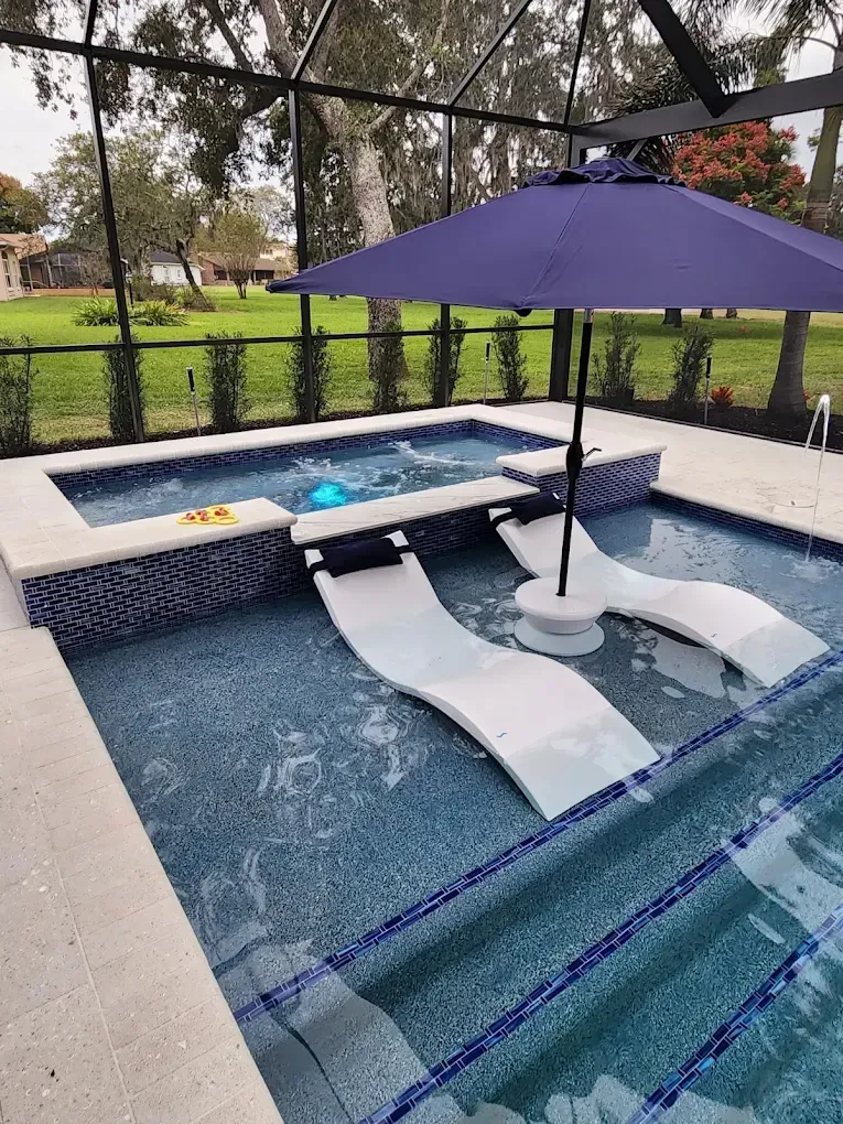 Backyard pool with submerged loungers, a hot tub, and a purple umbrella under a screened enclosure