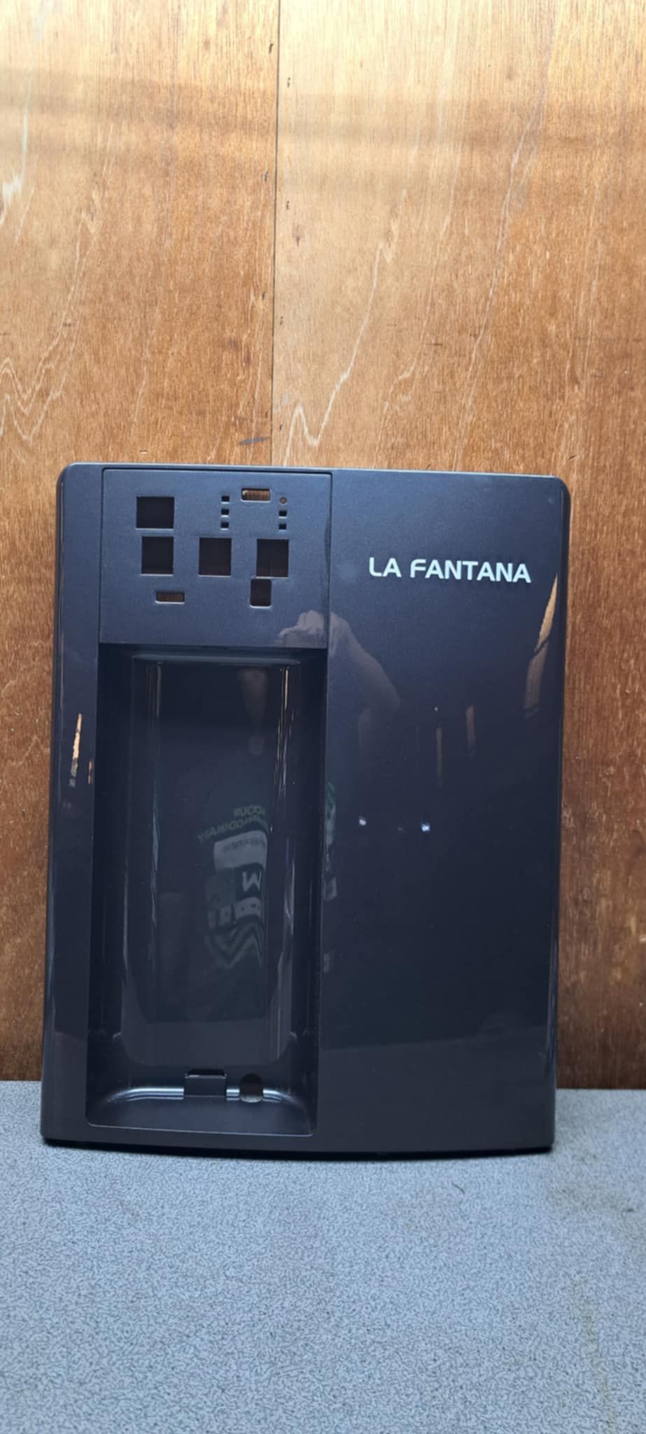 黑色桌上型飲水機，附瓶槽和前置出水口，靠牆放置。
