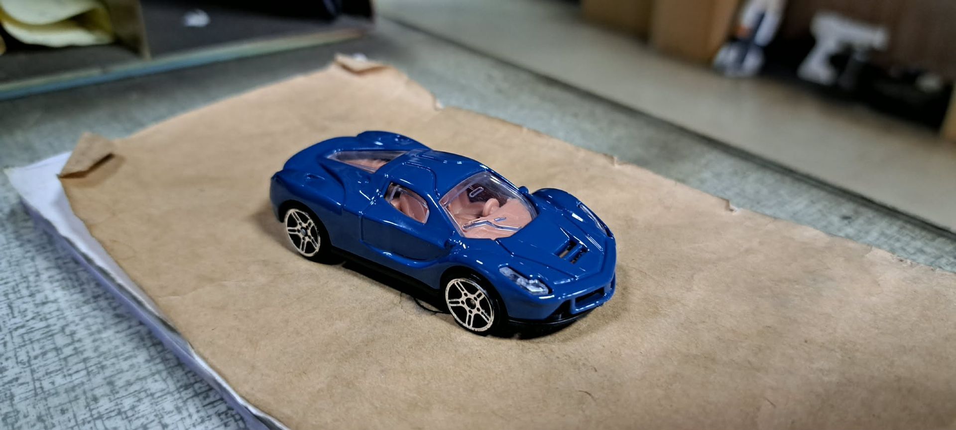 桌上放著一塊紙板，紙板上放著一輛藍色玩具賽車。
