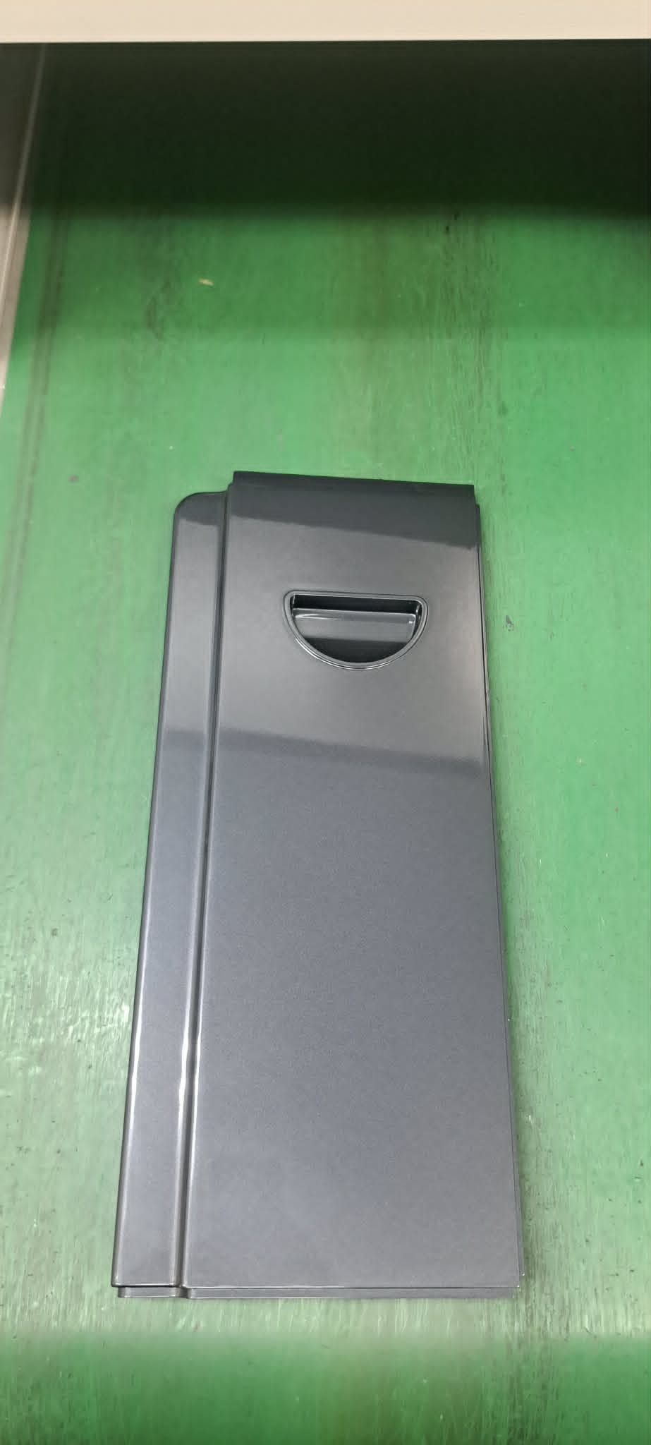 綠色牆面上安裝著一個灰色壁掛式設備，頂部附近有一個小槽。