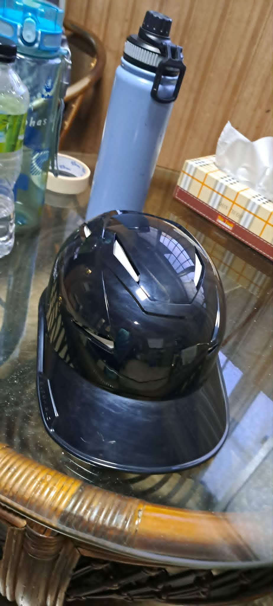 玻璃桌上放著一頂黑色摩托車頭盔，背景可以看到水瓶和保溫瓶。