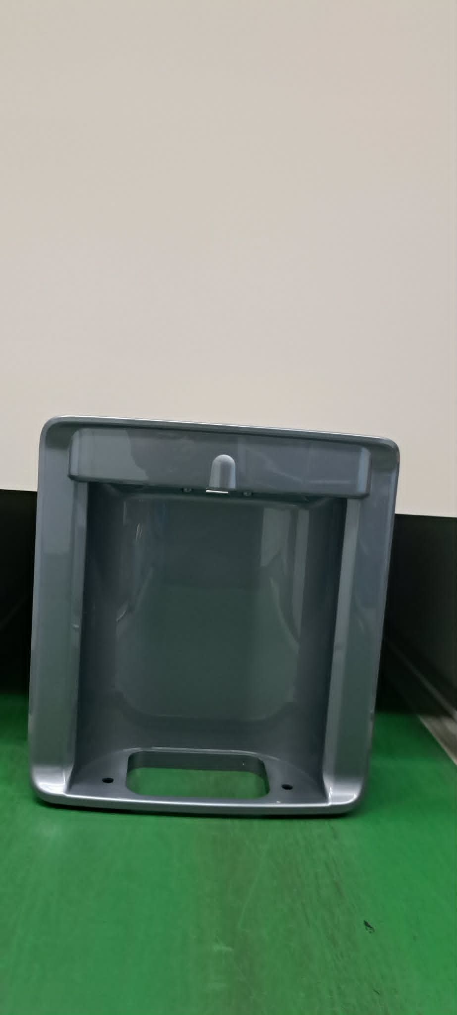 灰色塑膠容器放在淺色牆面前的綠色表面。