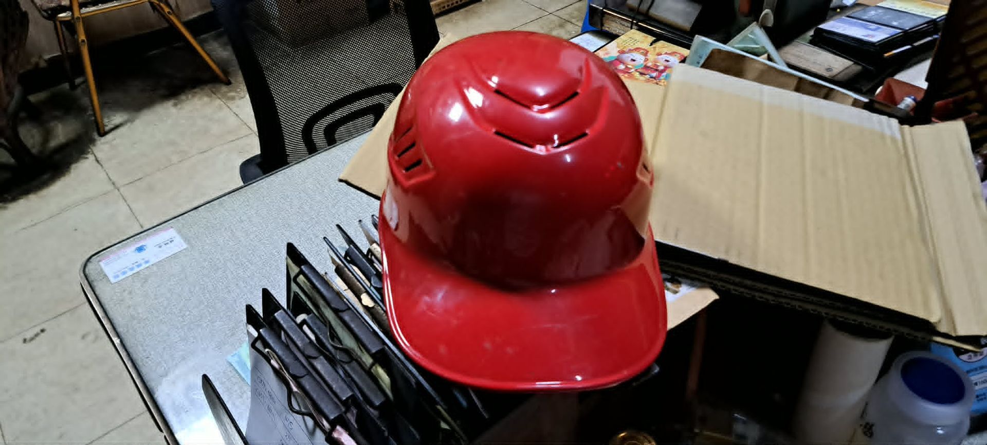 一頂紅色消防頭盔隨意地放在雜亂的工作台上，旁邊還有工具和紙箱。