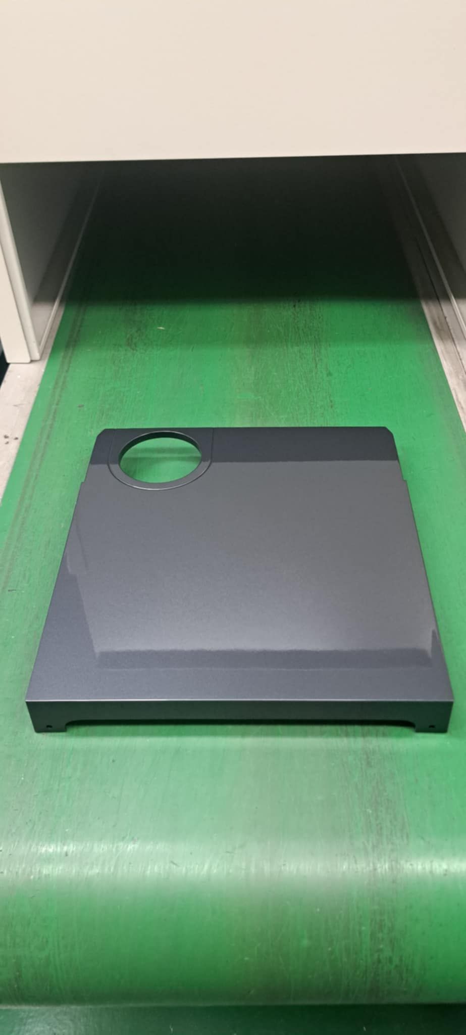 一台機器中，一個帶有圓形開口的灰色矩形裝置放置在綠色傳送帶上。