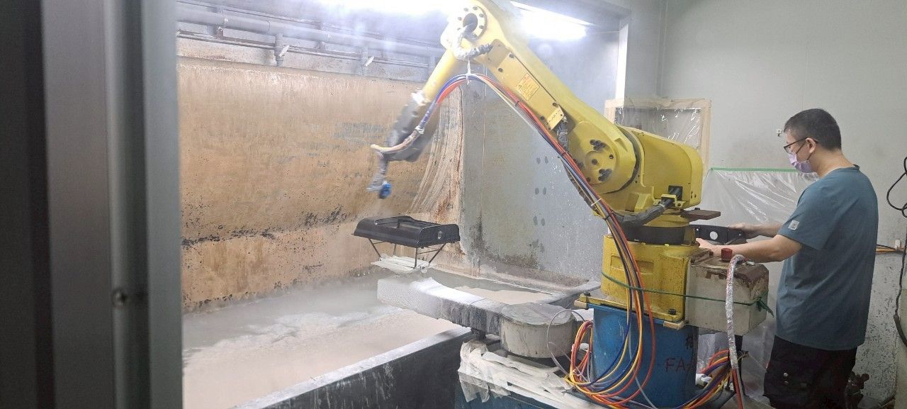 一名男子在車間操作黃色工業機械手臂,將材料噴塗到牆板上。