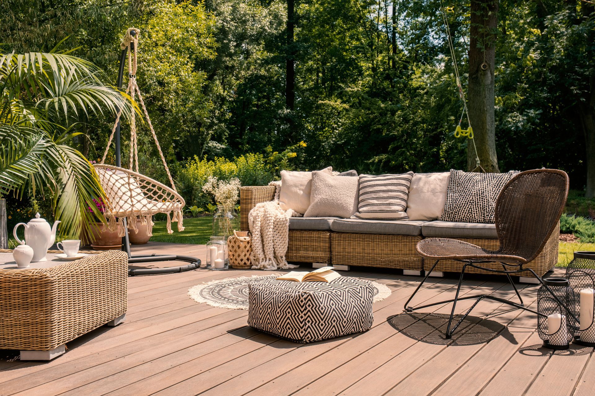 Wicker patio seating on a wooden deck in a lush garden, with a hanging chair and round coffee table