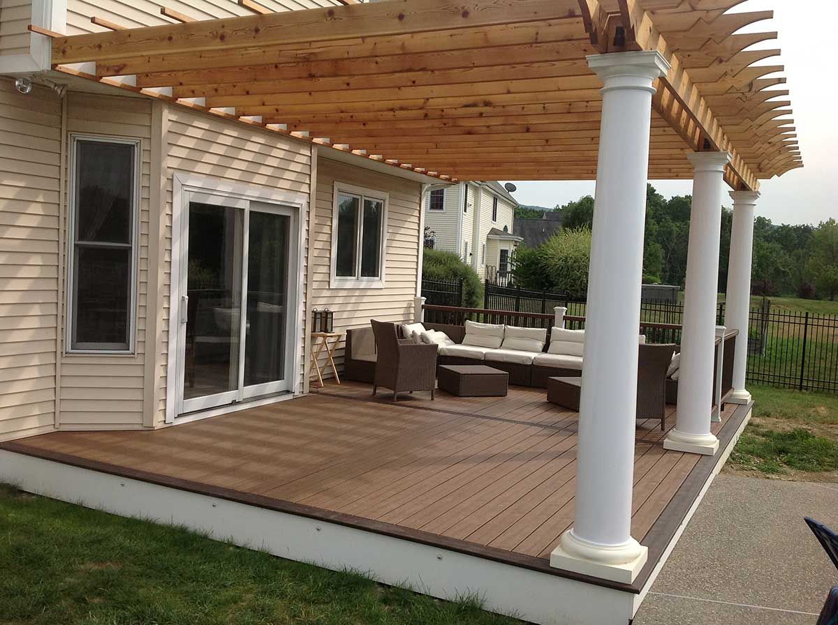 Back patio with wooden deck, pergola, white columns, and outdoor seating beside a house