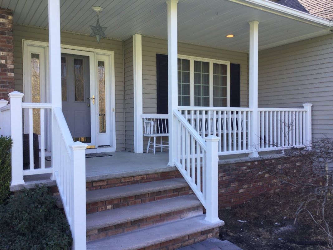 Front porch of a beige house with white railings, stairs, and a front door under a covered entry