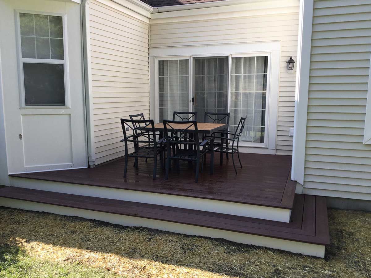 Backyard patio with a deck, outdoor table and chairs, and sliding glass doors on a house
