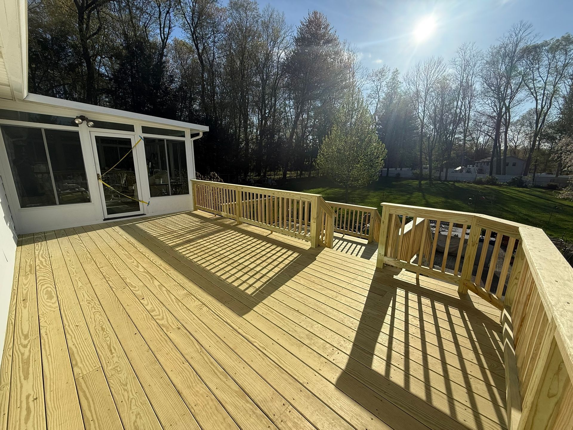 Wooden deck with white railing and black metal balusters overlooking a suburban front yard and street.