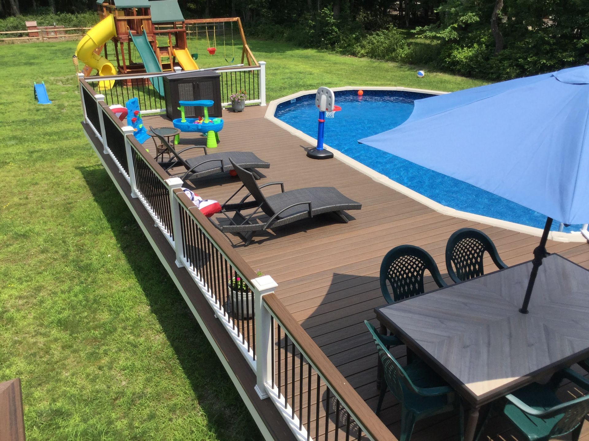 Backyard deck with white railing and stairs over dark retaining wall and brick patio